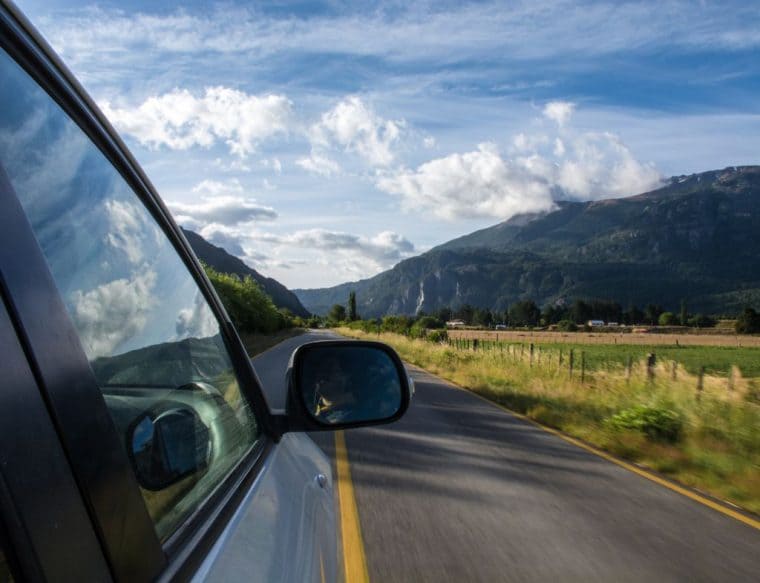 A car drives along a road with majestic mountains rising in the background. A car drives along a road with majestic mountains rising in the background.