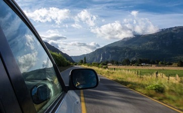 A car drives along a road with majestic mountains rising in the background. globalblog'