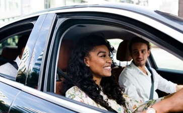 A man and woman are seated in the front of a car, both focused on the road ahead. globalblog'