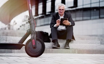A man in a suit casually sits on a scooter, blending professionalism with a playful mode of transportation. globalblog'