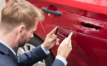 A man in a suit photographs his damaged car, capturing the aftermath of an unfortunate incident. globalblog'