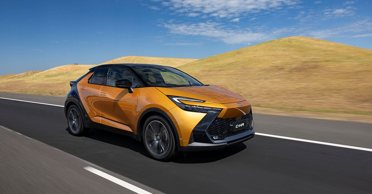 A new Toyota C-HR SUV driving along a scenic road, showcasing its modern design and performance.