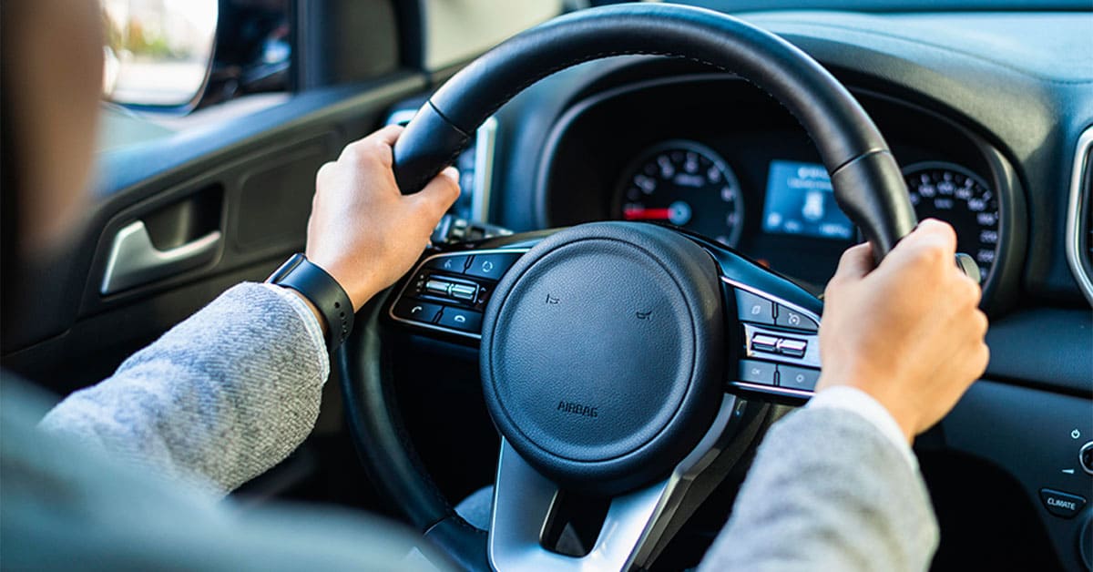 A person grips the steering wheel while driving a car, focused on the road ahead.