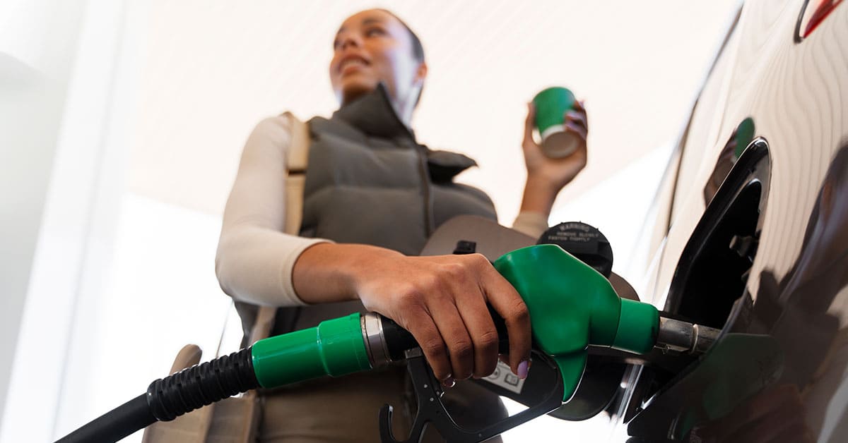 A woman is refueling her car at a gas station, holding the fuel nozzle.