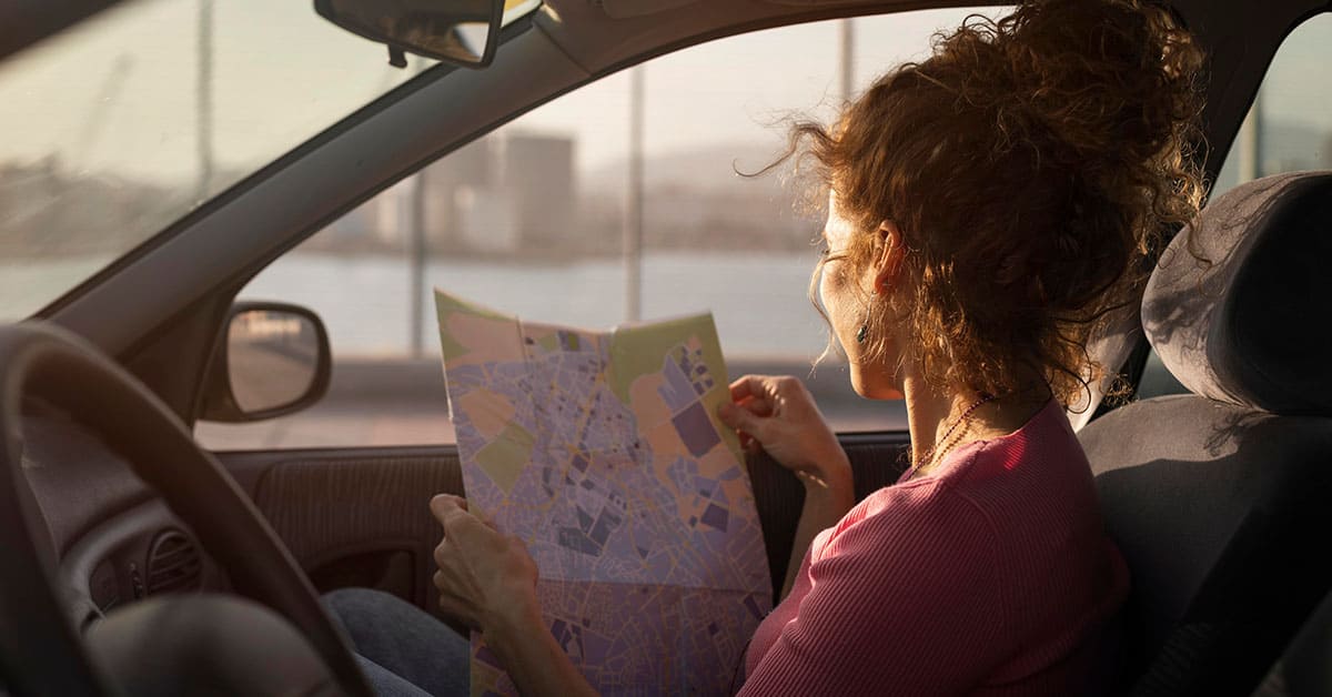 A woman sits in a car, studying a map with a focused expression.