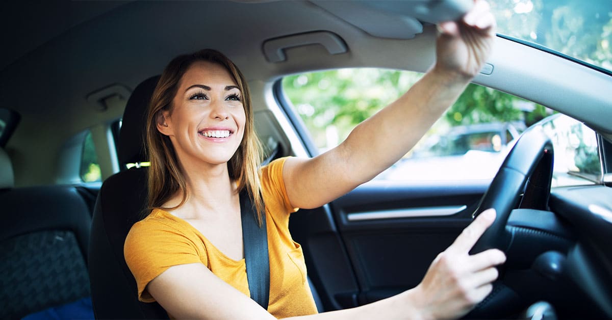 A woman smiles while driving her car, showcasing a joyful moment behind the wheel.