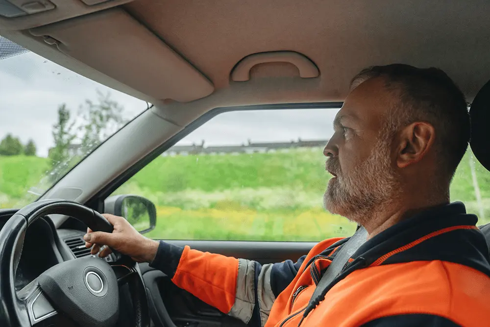 Driver in high-visibility jacket driving a car.