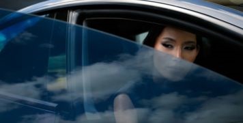 Woman in car driver seat opening the door. She is partially obscured by the window which has Oridon Ceramic Window Tint applied.