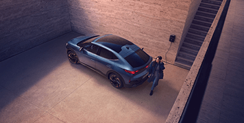 Woman approaches Cupra Tavascan electric SUV coupe parked and charging in basement