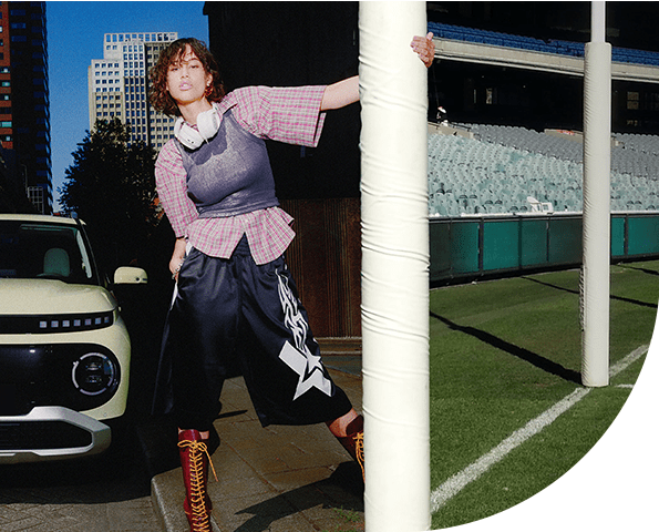 Split screen of a Hyundai INSTER parked in the city with a goal post for a lamp post and the MCG on the other side.