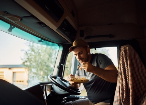 A driver overcomes fatigue by taking a break and eating in his cab.