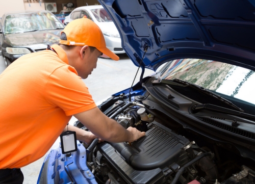 A man in an orange top and hat repairs a car for a commute