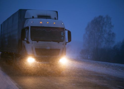 A lorry drives through dark wintry conditions with headlights on