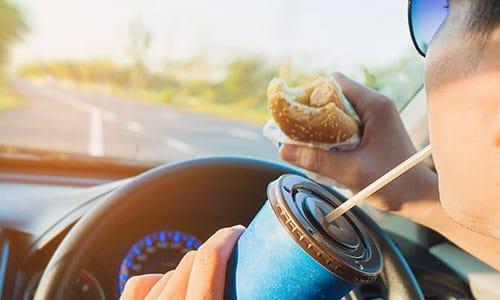 Man is dangerously eating and drinking while driving a car