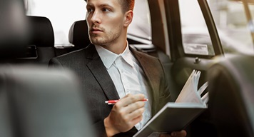 Man writing in a notebook in the back seat of a vehicle