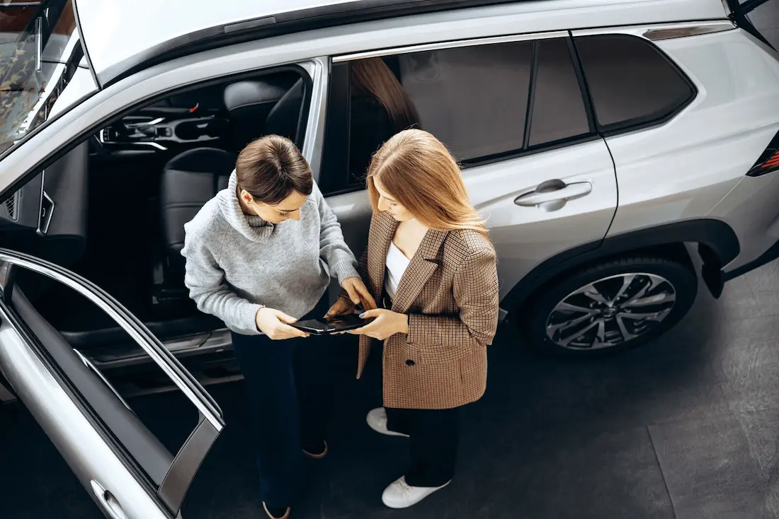 two women standing next to car
