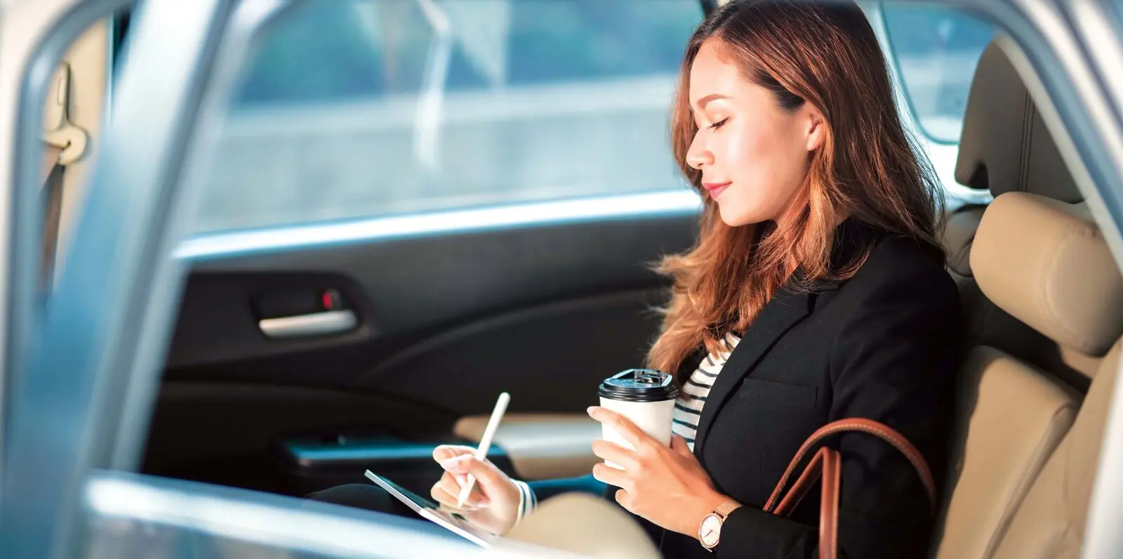 Woman in backseat of car with coffee and a tablet