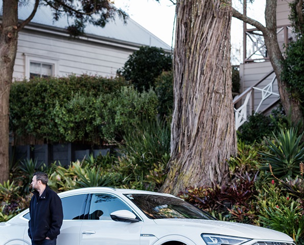 male-standing-next-to-parked-ev-outside-home male-standing-next-to-parked-ev-outside-home