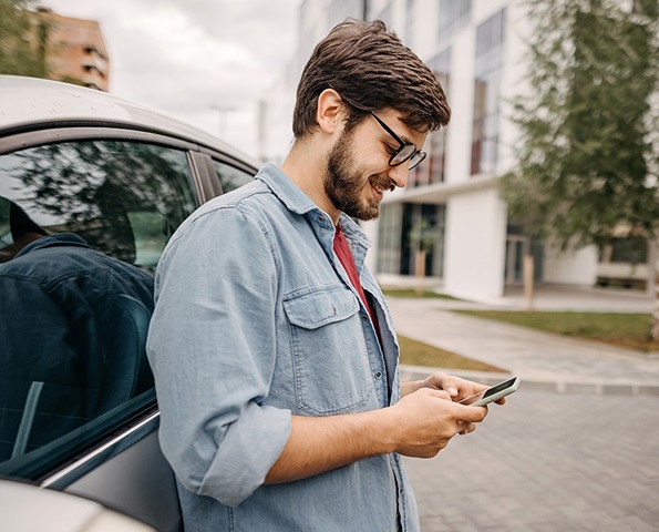man-smiling-at-phone-next-to-car