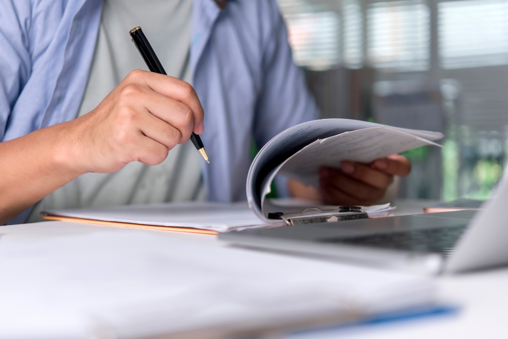 benefits of streamlined fleet administration: Close-up of hands reviewing documents and paperwork on a desk next to a laptop, suggesting organised fleet or business administration.