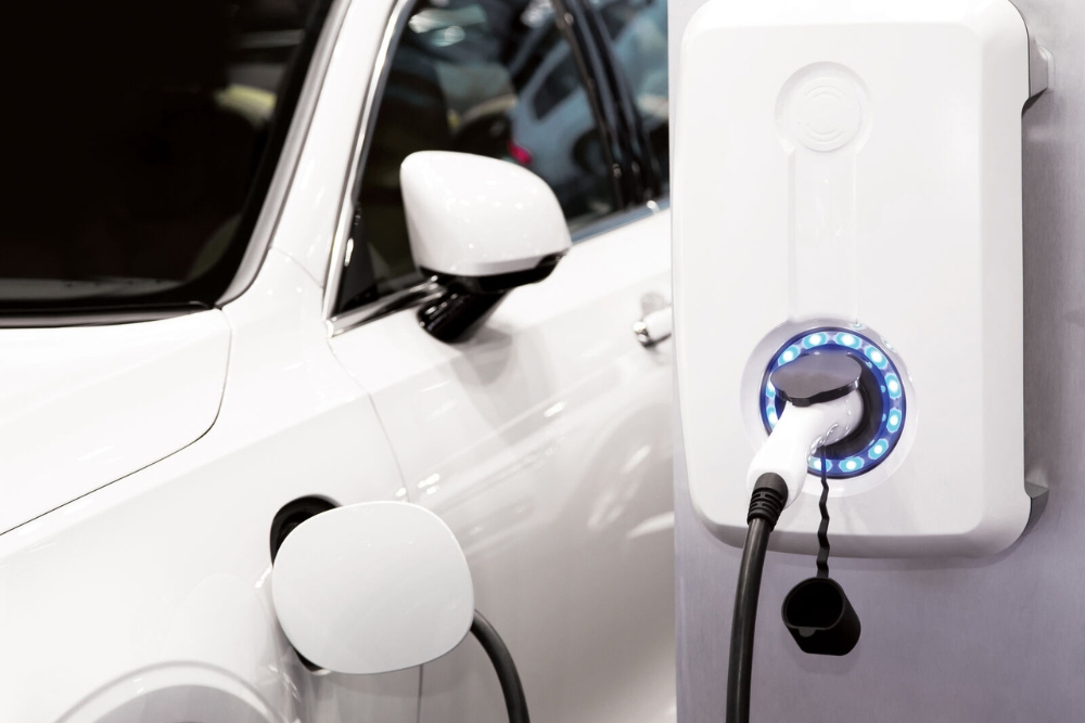 Close-up of a white electric car plugged into a modern home EV charger with a glowing blue LED ring.
