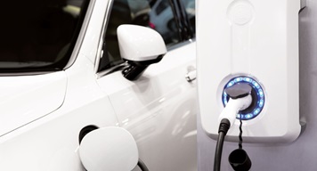 Close-up of a white electric car plugged into a modern home EV charger with a glowing blue LED ring.
