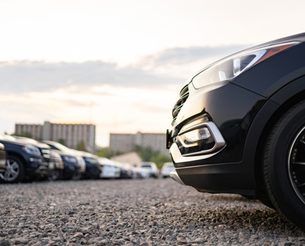 EV Fleet maintenance: Several cars parked in a row on gravel with a close-up view of the front wheel of a black vehicle.