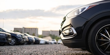 EV Fleet maintenance: Several cars parked in a row on gravel with a close-up view of the front wheel of a black vehicle.