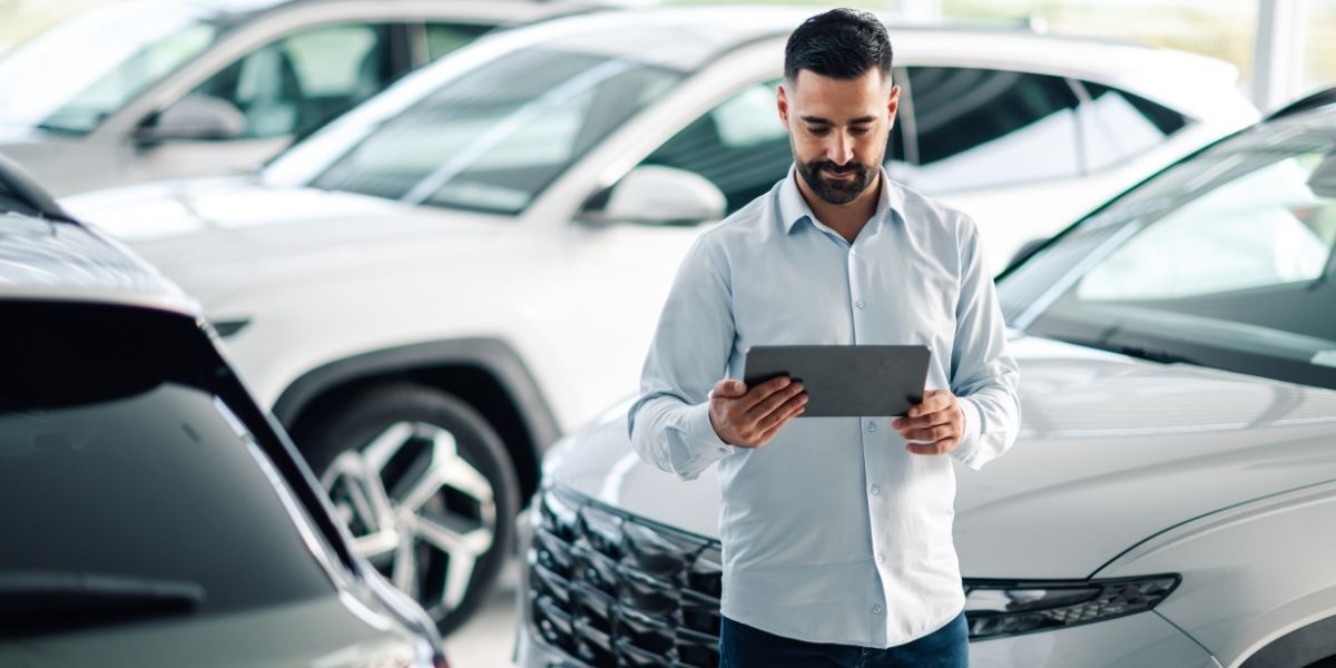 how do companies improve fleet efficiency A man in a light blue shirt browsing a tablet whilst standing among a row of cars in a bright showroom.