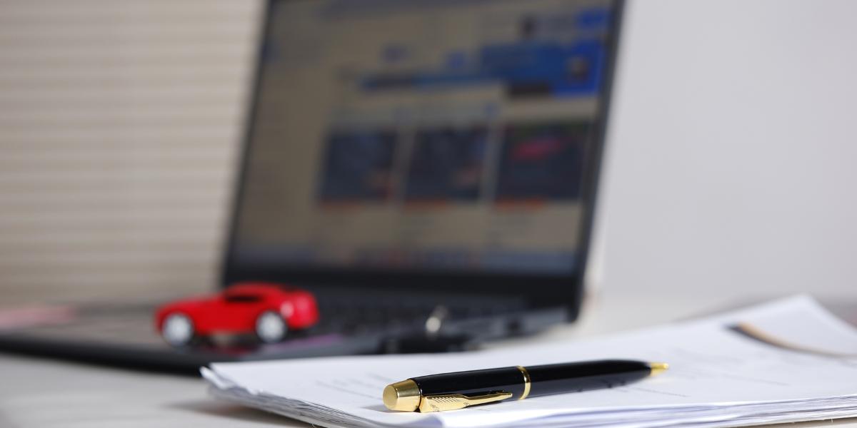 P11D Company Car changes: A small red toy car sitting on a laptop keyboard in the background, with a black and gold pen resting on a stack of paperwork in the foreground.