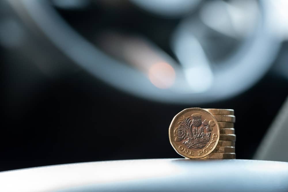 rising fleet vehicle leasing costs Stacked pound coins in front of blurred car steering wheel
