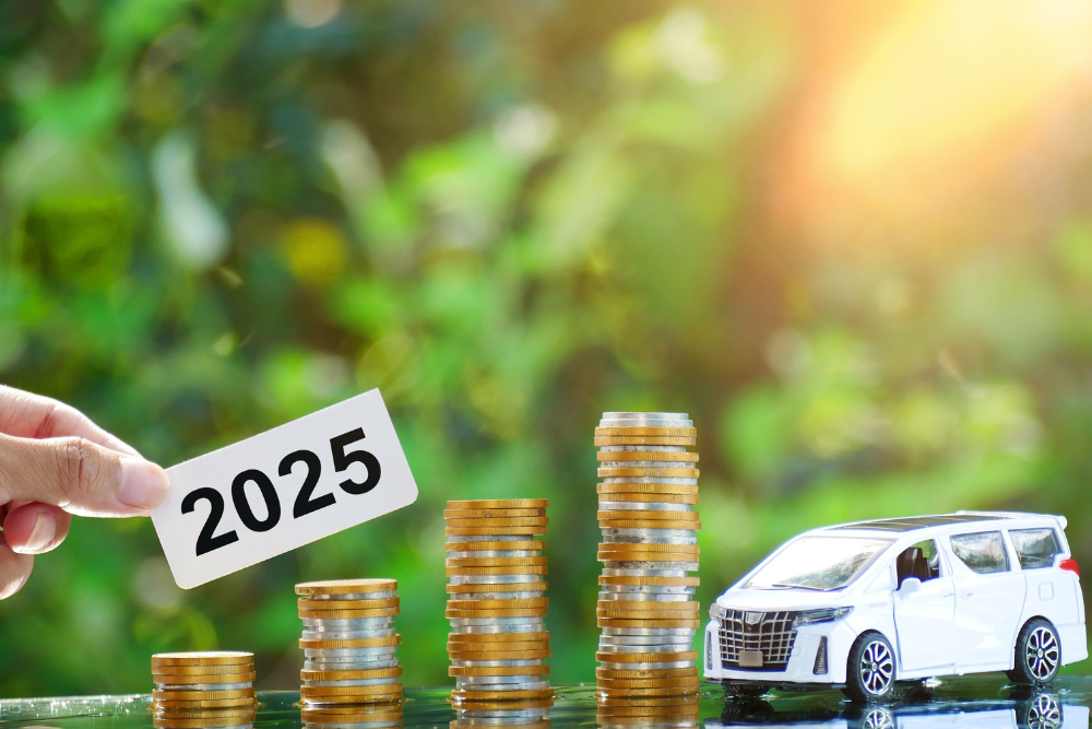 Alt text: Stacks of coins beside a toy car with a hand holding a 2025 sign, symbolising how the 2025 Budget could influence motoring costs and vehicle expenses.