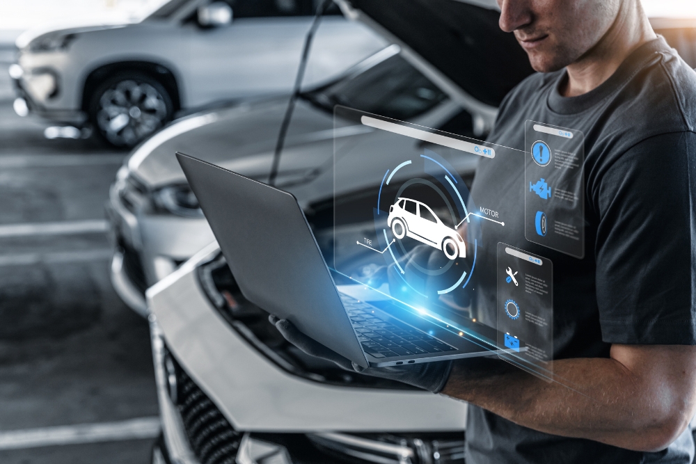 UK fleet management: A mechanic using a laptop with digital car diagnostics projected above the screen in a workshop.