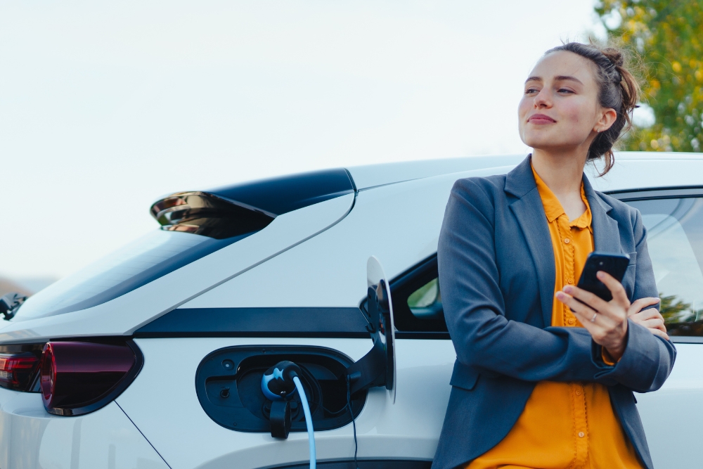 woman ev phone a woman standing next to an EV on her phone